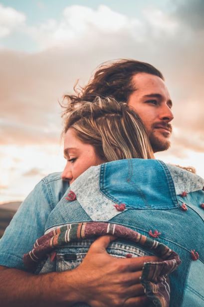 Couple sharing a warm embrace in denim jackets against a sunset sky