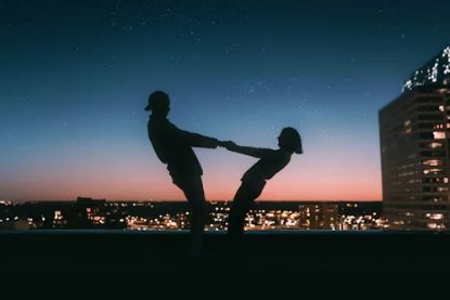 Silhouette of a playful couple against a city skyline at sunset